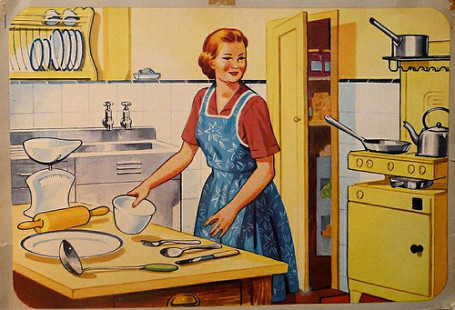 Female smiling with an apron and standing in front of cooking equipment in a kitchen