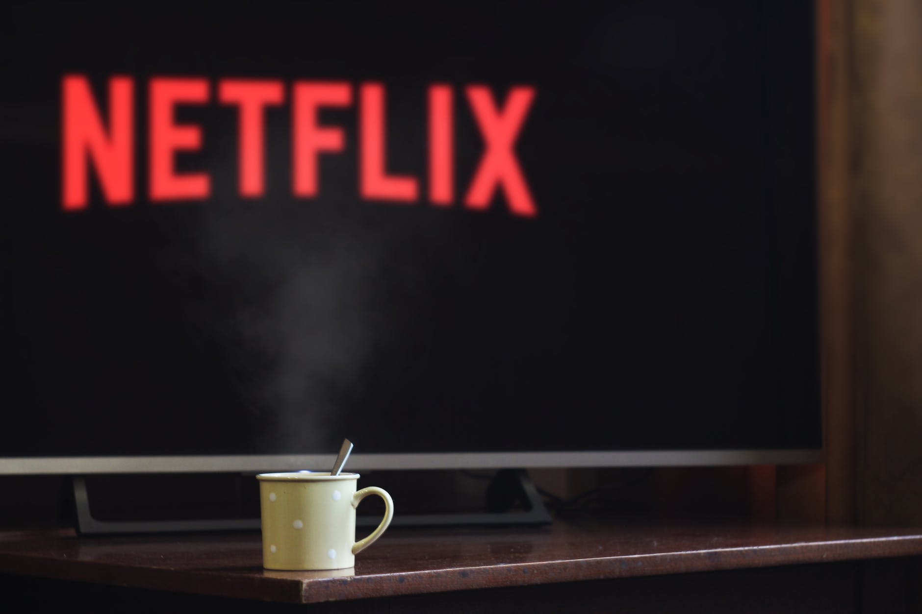 Steaming cup of hot beverage with a wide flat-screen TV showing Netflix logo in the background
